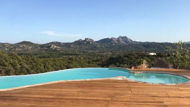 A wooden deck with a swimming pool and a mountainous landscape in the background. - Villa La Mendula (Arzachena)
