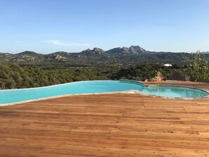 A wooden deck with a swimming pool and a mountainous landscape in the background.