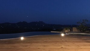 A wooden deck with a view of mountains and city lights in the background. - Villa La Mendula (Arzachena)