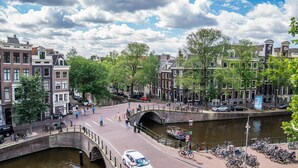 A canal-side walkway with historic buildings, a bridge, and a boat tour. - Hotel Frank since 1666 (Amsterdam)