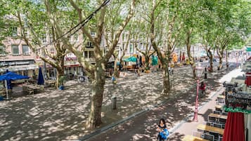 Una zona peatonal arbolada con mesas al aire libre y diversas tiendas.