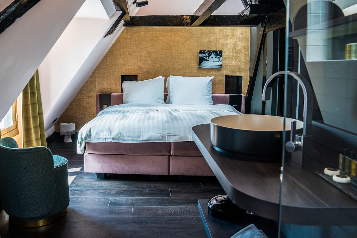 A modern bedroom with a loft-style design, featuring a bed with white bedding, a small bedside table, and a unique green chair.