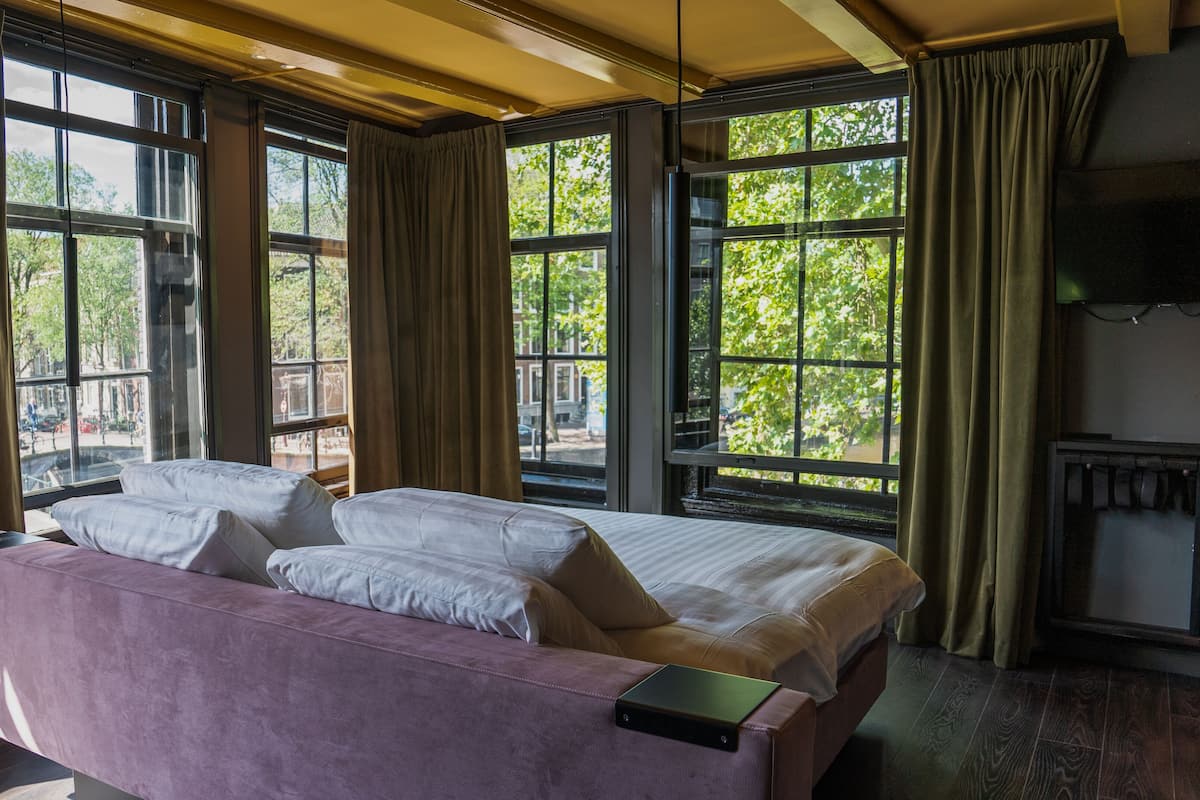 A room with a bed, a sofa, and large windows with curtains.