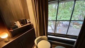A cozy corner with a cushioned chair, a small round table, a lamp, and a window with a view of the street and trees. - Hotel Frank since 1666 (Amsterdam)