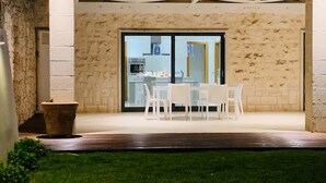 A patio area with a table and chairs, a stone wall, and a view of the kitchen through glass doors.