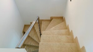 A staircase with a metal handrail and beige steps. There are two square light fixtures on the ceiling.