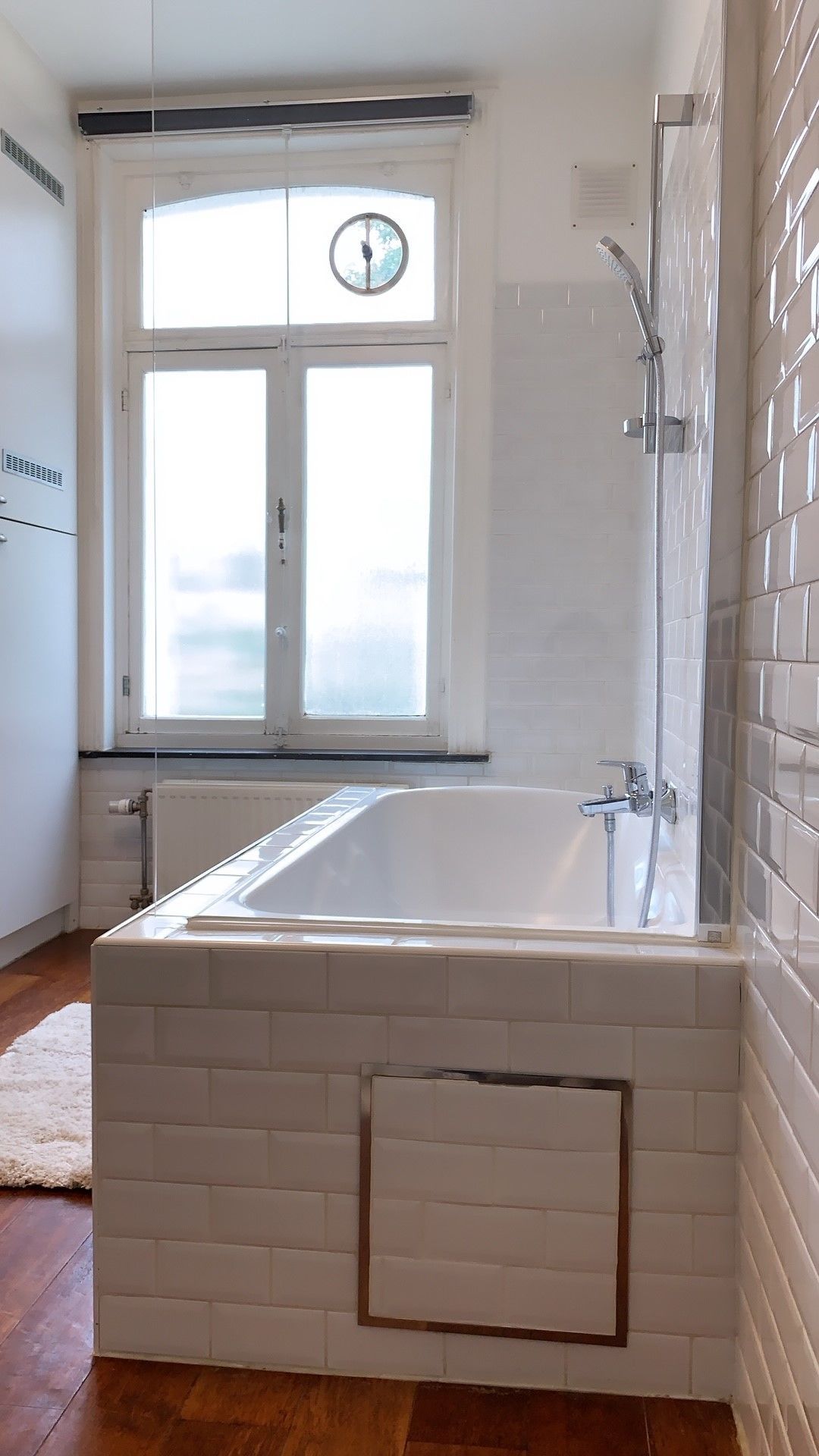 A bathroom with a bathtub, a window, and a shower.