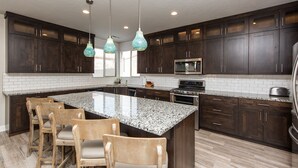A kitchen with dark wood cabinets, a granite countertop, and a central island with bar stools. - Vermillion Oasis: Luxury 6BR/7BA Home near Zion. Private Pool & Resort Amenities (Santa Clara)