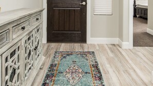 A hallway with a dark wooden door, a white wall, and a patterned rug. - Vermillion Oasis: Luxury 6BR/7BA Home near Zion. Private Pool & Resort Amenities (Santa Clara)
