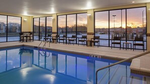 A swimming pool with a view of the sunset through large windows, surrounded by chairs and tables. - Courtyard by Marriott Kansas City Olathe (Olathe)