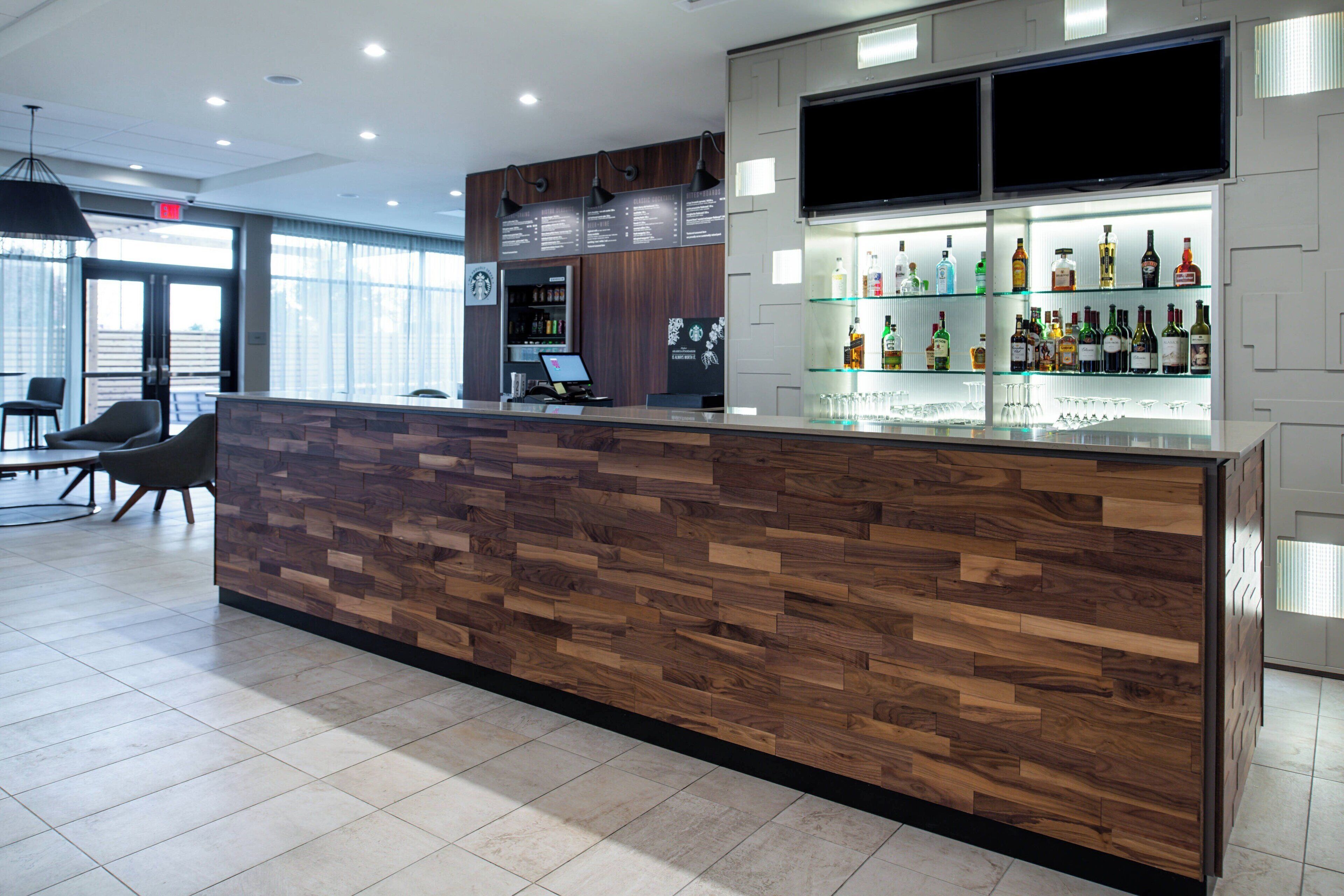 Een moderne receptie met een houten balie, een bar met diverse drankflessen en een zithoek met stoelen.