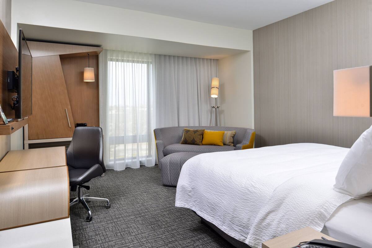 Una habitación de hotel con una cama, un escritorio, una silla, un sofá y una lámpara.