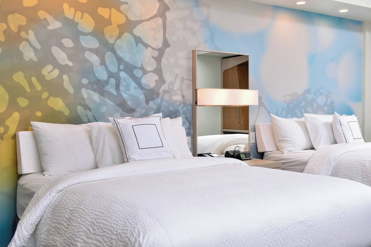 Habitación de hotel con dos camas, un espejo grande y una pared con un diseño abstracto y colorido.