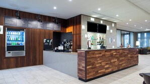 A modern bar area with a wooden counter, a beverage dispenser, and a flat-screen TV. - Courtyard by Marriott Kansas City Olathe (Olathe)
