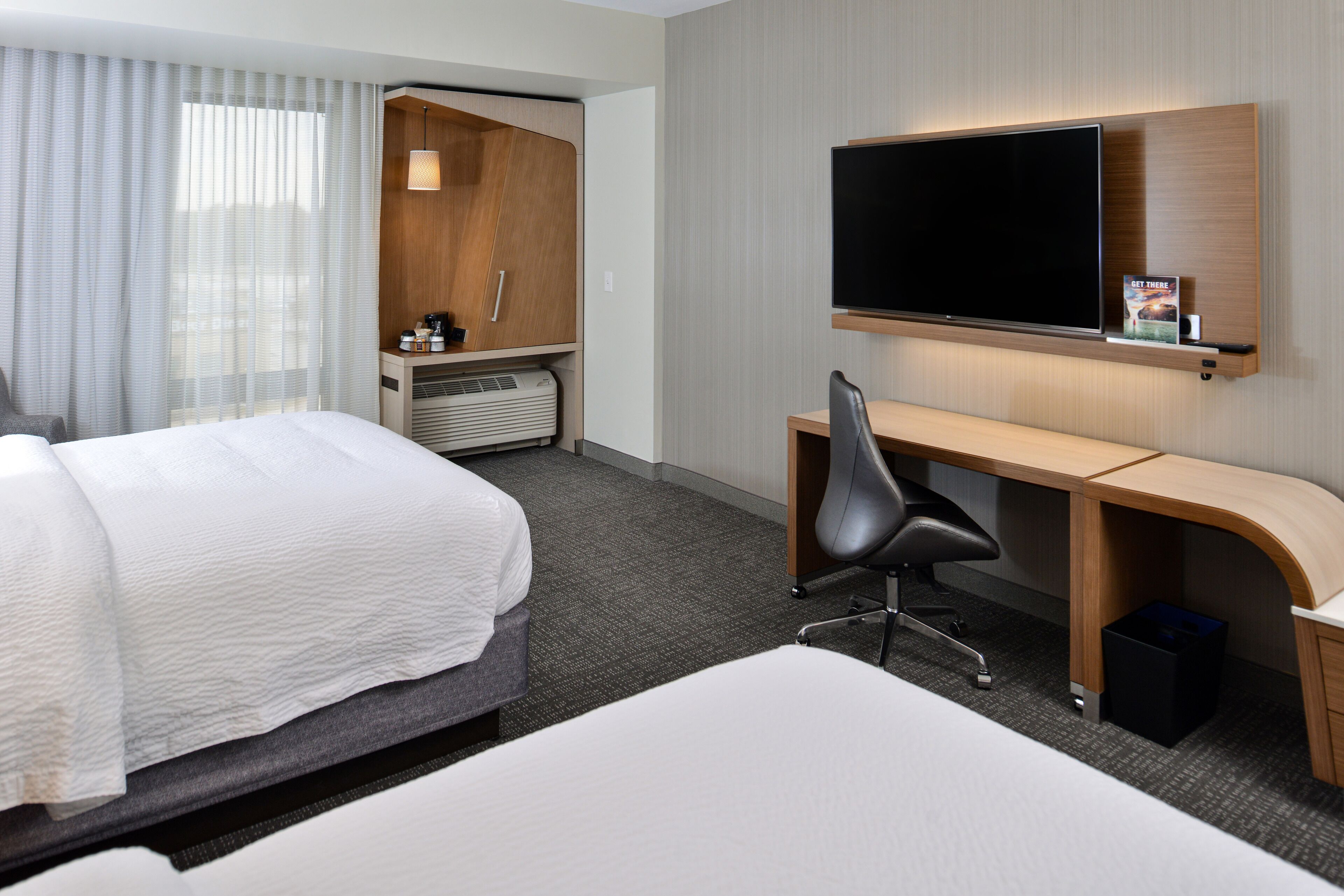 A hotel room with a bed, a desk, a chair, a TV, and a minibar.