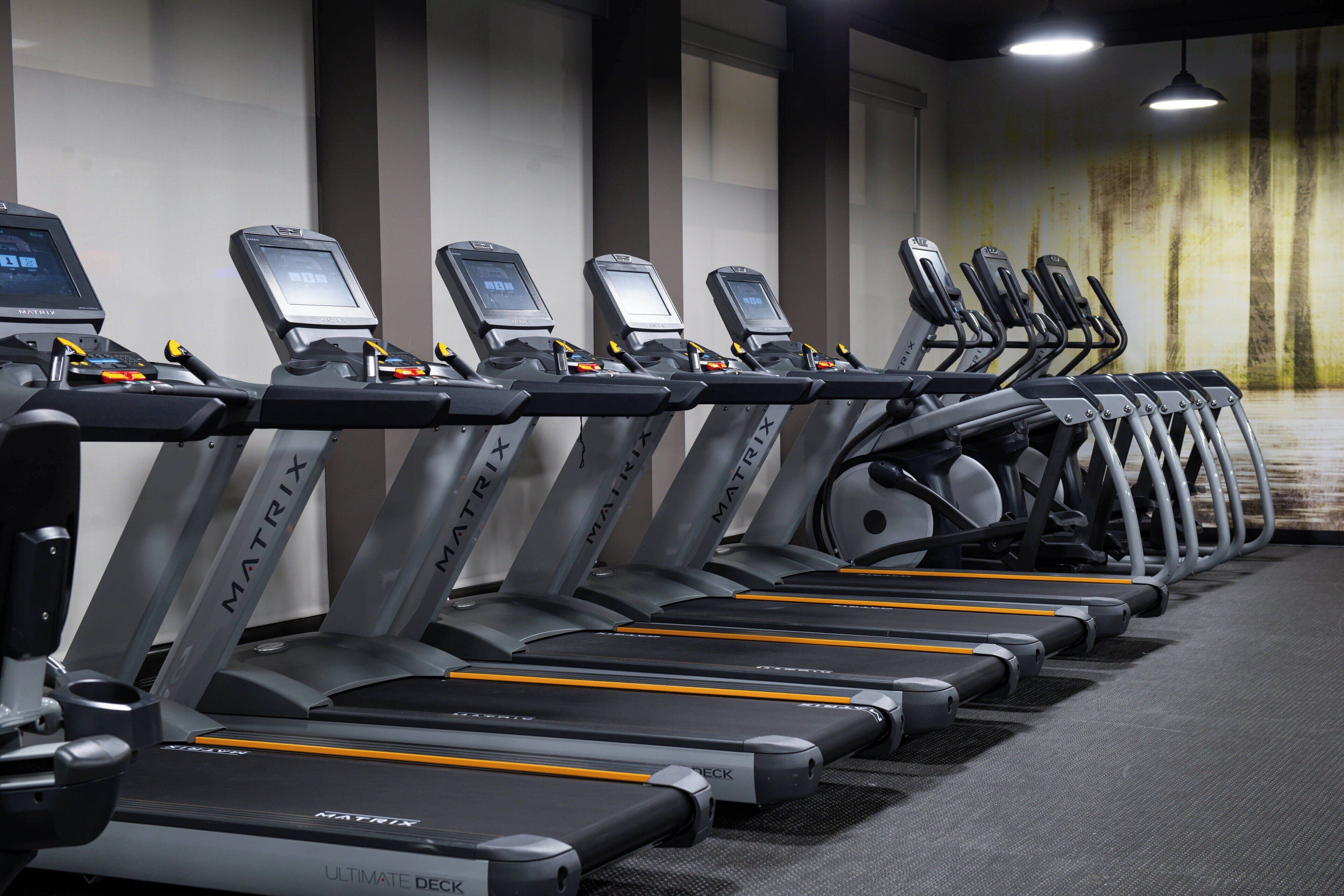 Une rangée de tapis de course MATRIX dans une salle de sport, avec un tapis gris et un mur orné d’un motif texturé.