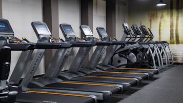 Une rangée de tapis de course MATRIX dans une salle de sport, avec un tapis gris et un mur orné d’un motif texturé.