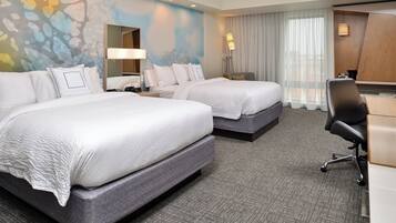 A hotel room with two beds, a desk, a chair, a lamp, and a large window with curtains.