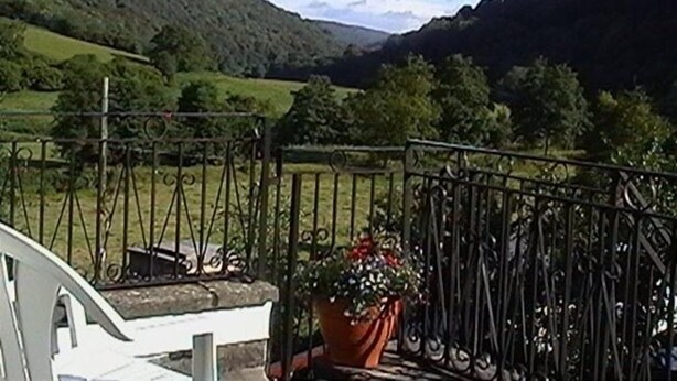 A balcony with a wrought iron railing overlooking a valley with green fields and hills.