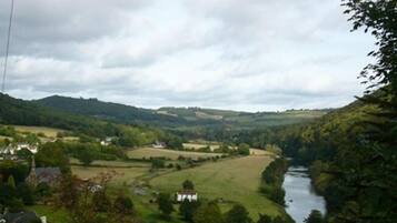 A rural landscape with a river, houses, and rolling hills.