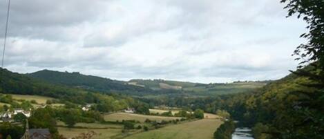 A rural landscape with a river, houses, and rolling hills.
