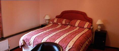 A bedroom with a bed, two bedside tables, a chair, and a radiator.