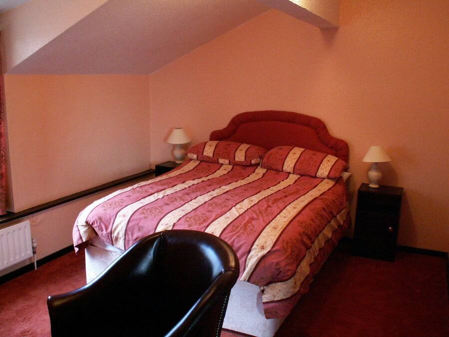 Un dormitorio con cama, dos mesitas de noche, una silla y un radiador.