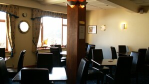 A dining area with tables and chairs, a wooden pillar, and a window with curtains.