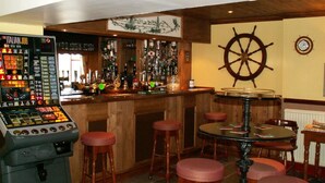 A bar area with a jukebox, stools, a round table, and a ship's wheel decoration.