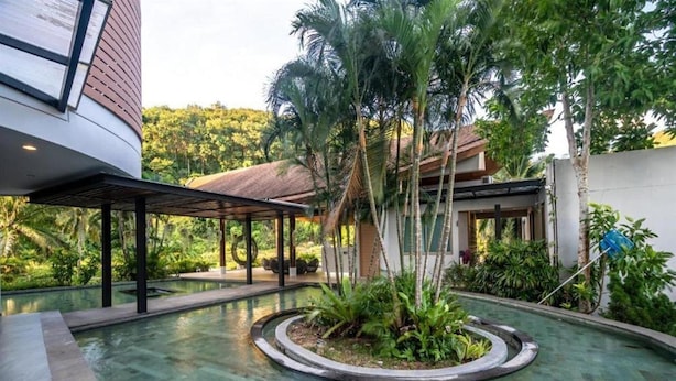 A modern building with a covered outdoor area and a circular pool surrounded by tropical plants. - The Ark By Veloche Group (Karon)