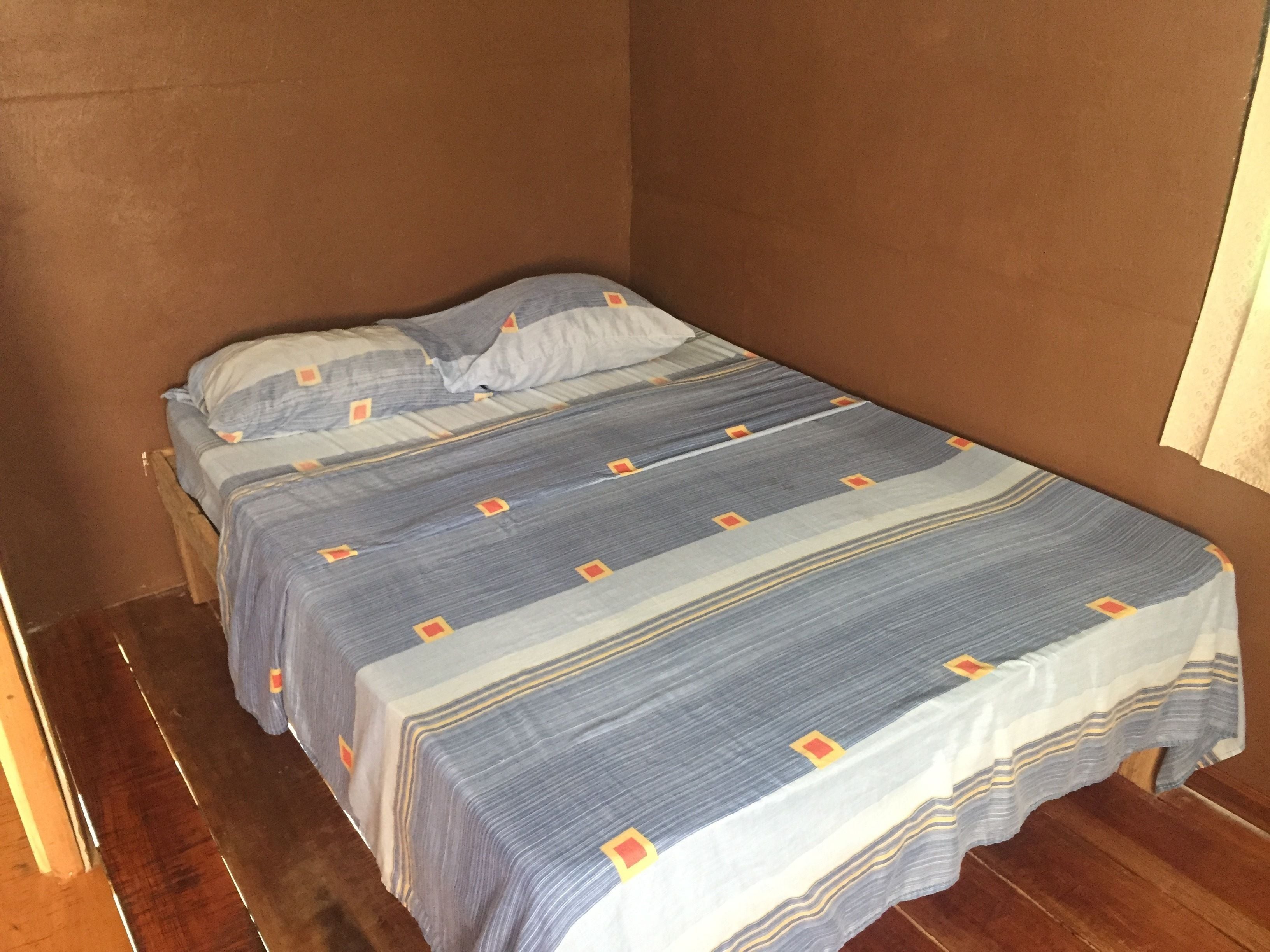 A single bed with a striped bedspread and pillows in a room with wooden flooring and brown walls.