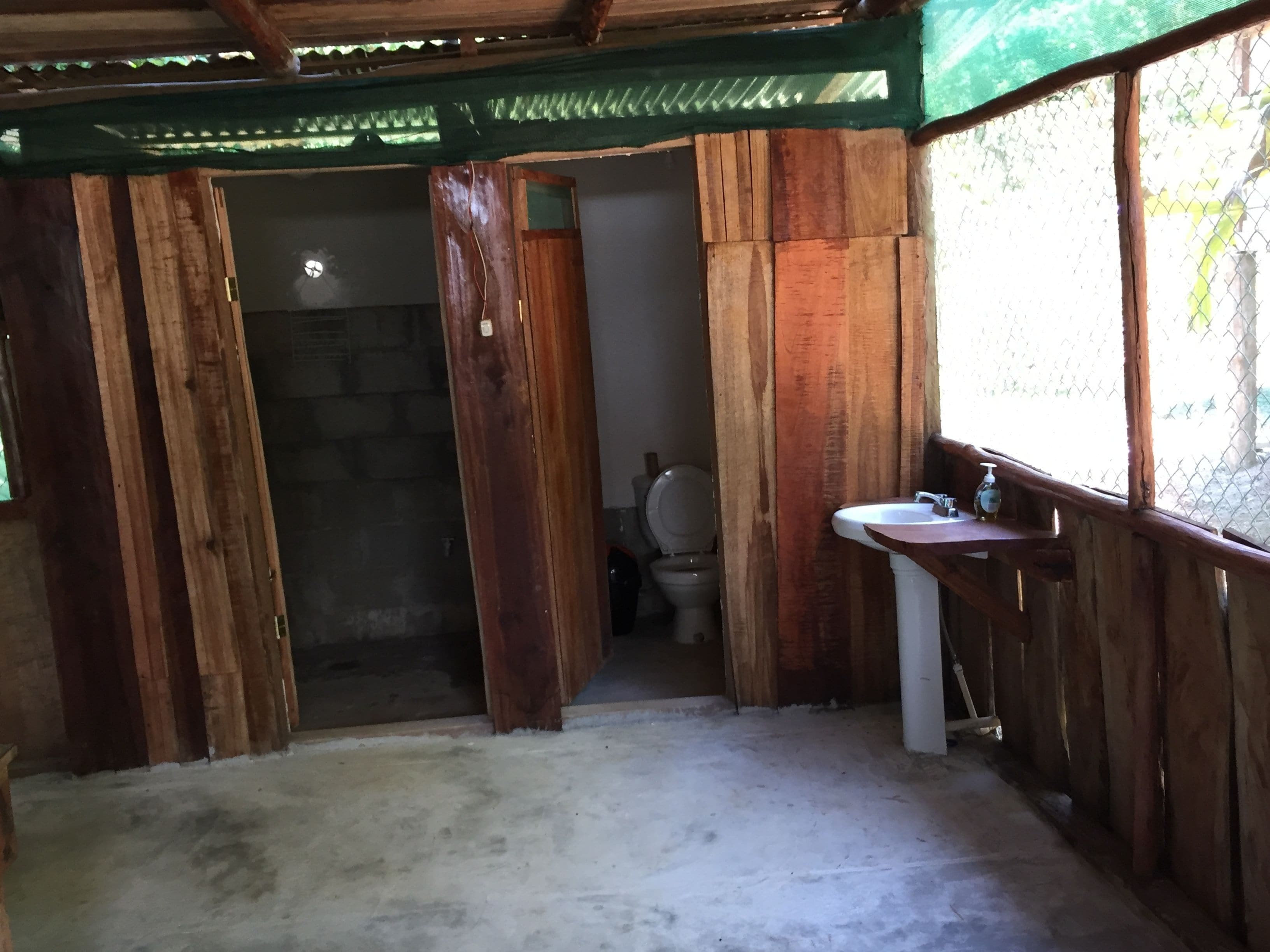 A rustic bathroom with wooden walls, a toilet, and a sink with a soap dispenser.