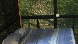 A bed with a striped blue and white bedspread and pillows, positioned under a window with a view of trees.