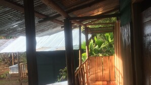 A covered wooden deck with a metal roof, surrounded by greenery.