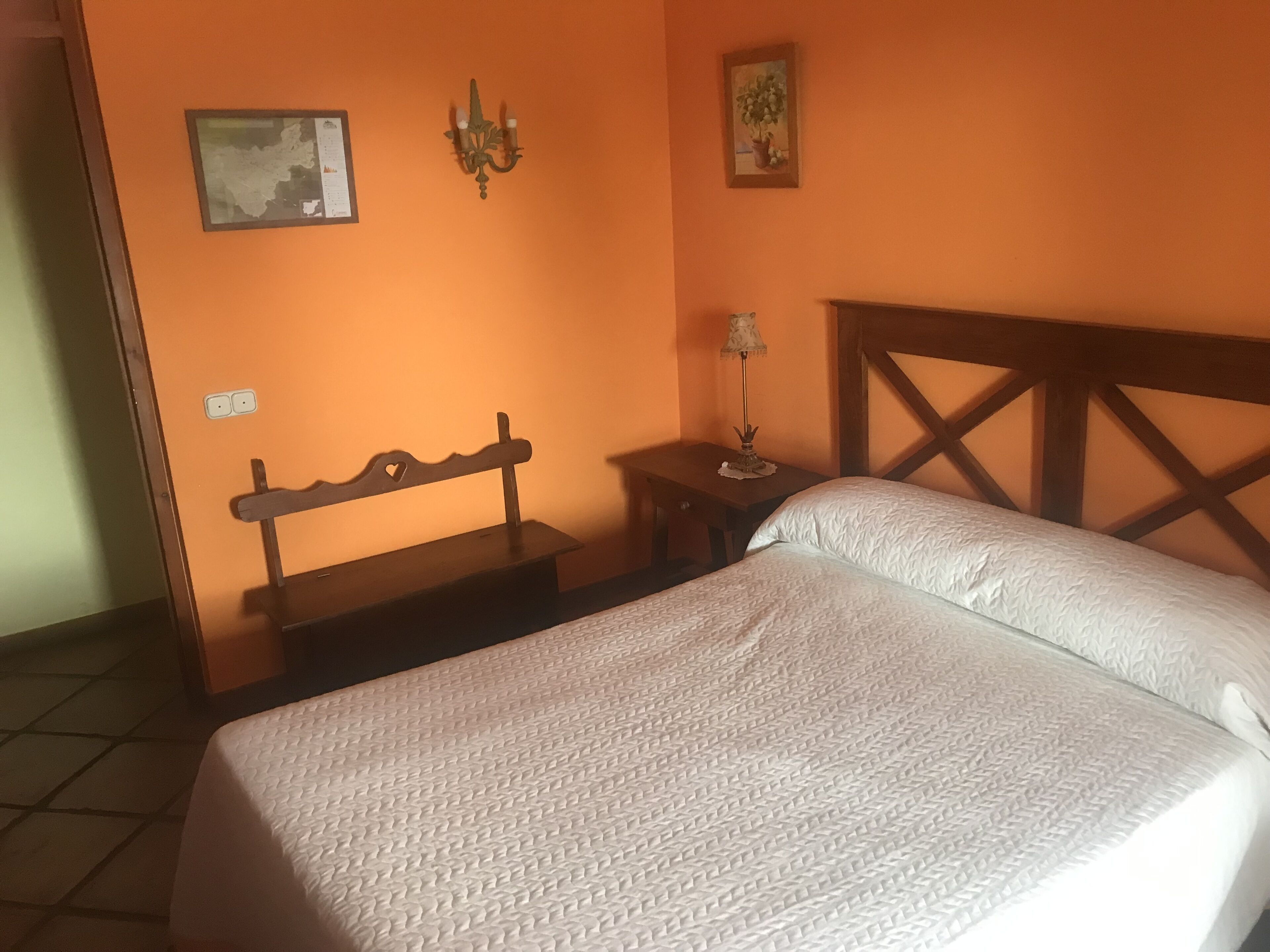 A bedroom with a bed, a nightstand, a wall-mounted lamp, and a small table.