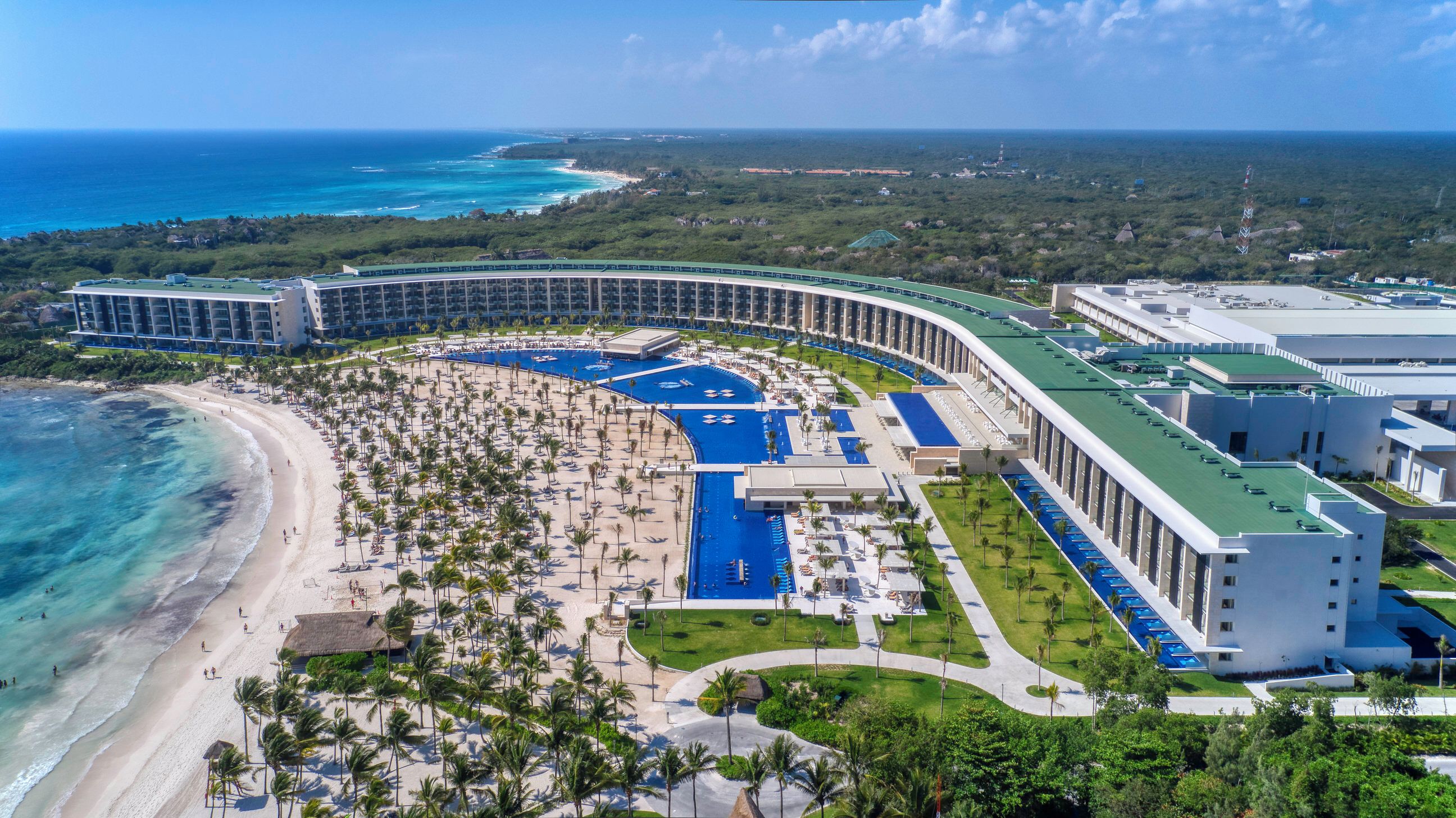 Vista aérea de un resort con zona de piscina curva, acceso a la playa y varios edificios.