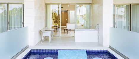 Una piscina interior moderna con suelo de mosaico azul, una zona de estar con mesa y sillas, y una bañera grande.