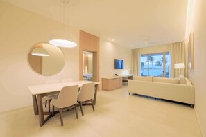 Una habitación de hotel moderna con comedor, sofá, televisor y vistas a palmeras.