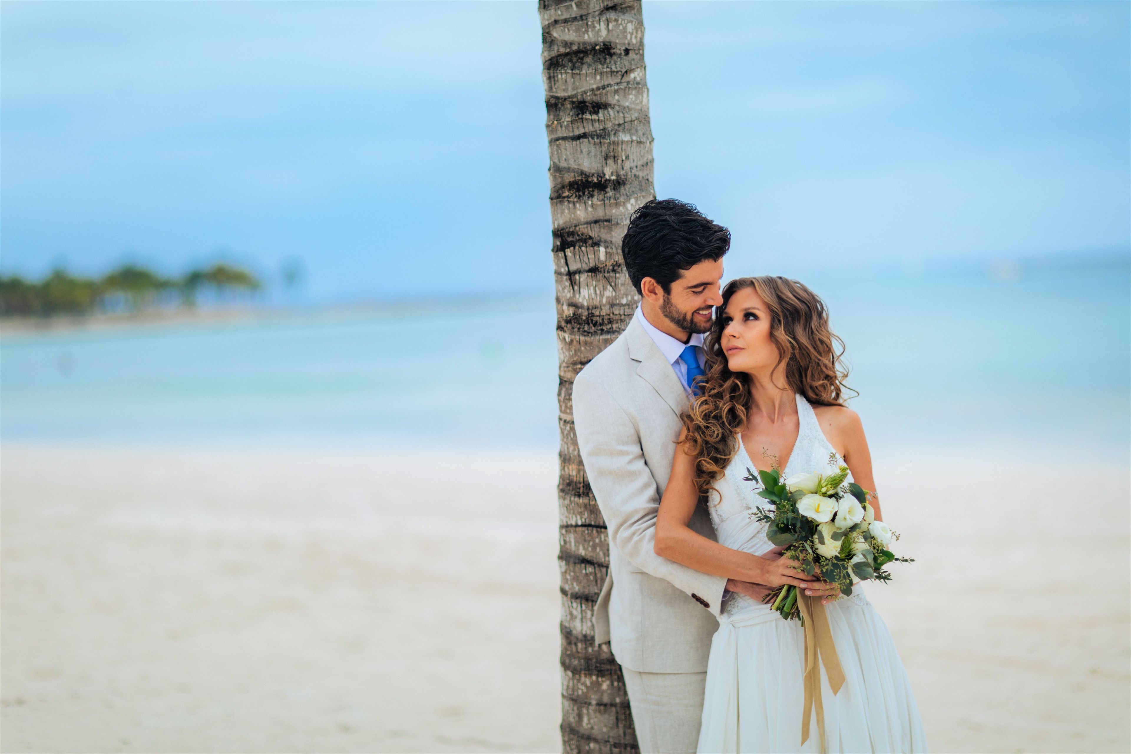 Una pareja en la playa, con una palmera y el océano al fondo.