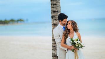 Una pareja en la playa, con una palmera y el océano al fondo.