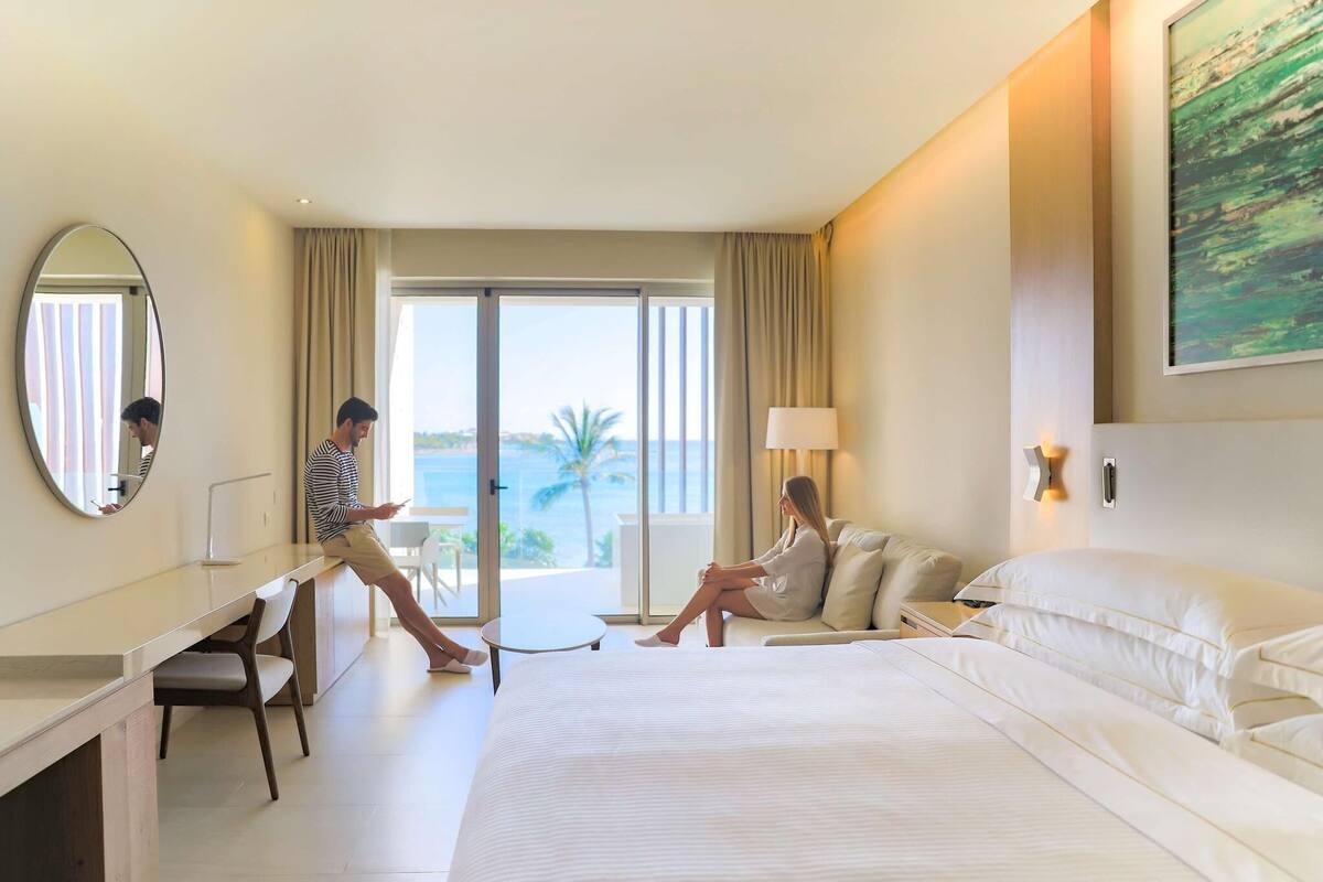 Ein Hotelzimmer mit einem großen Bett, einem Schreibtisch, einem Sessel und Meerblick.