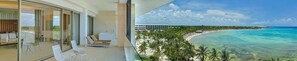 A balcony with a glass door leading to a room with a sofa and chairs, overlooking a beach and ocean. - Barcelo Maya Riviera (Xpu-Ha)