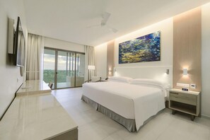 A hotel room with a large bed, a desk, a chair, a TV, a painting, and a balcony with a view. - Barcelo Maya Riviera (Xpu-Ha)