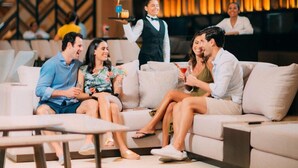 Un gruppo di persone sedute su un divano in una zona relax moderna, con un grande schermo che mostra una vista urbana.