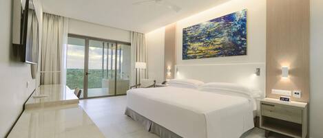 A hotel room with a large bed, a desk, a chair, a TV, a painting, and a balcony with a view.