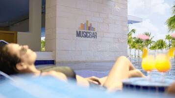 Una persona relajándose en una piscina con un cartel de 'MUSICBAR' al fondo.