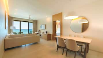 Una habitación de hotel moderna con sofá, mesa de comedor y sillas. Hay un ventanal con vista al mar.