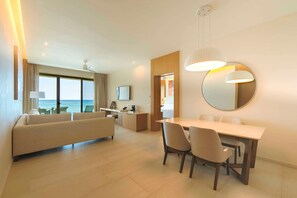 A modern hotel room with a sofa, dining table, and chairs. There is a large window with a view of the sea. - Barcelo Maya Riviera (Xpu-Ha)