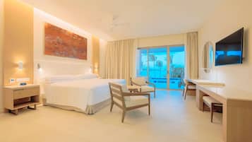 Habitación de hotel con cama, escritorio, silla, televisión y balcón con vistas.