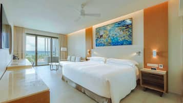 Una habitación de hotel moderna con una cama grande, un escritorio, un televisor de pantalla plana, un ventilador de techo, un cuadro y vista al océano.